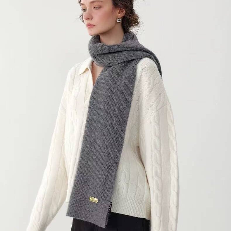 Person wearing a gray 100% cashmere luxury scarf over a white sweater on a plain background
