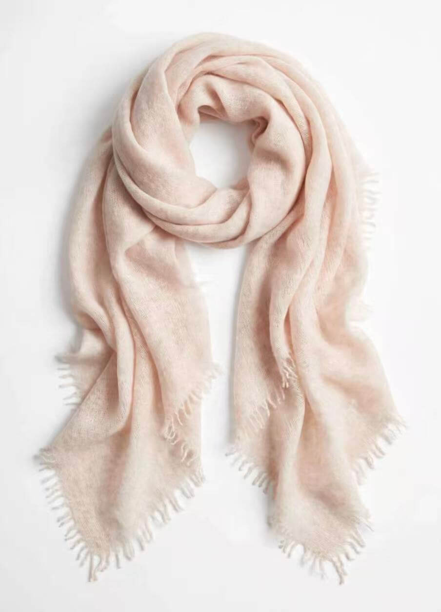 A soft, pale blush pink cashmere scarf with fringed edges, draped in a loose loop against a clean white background.