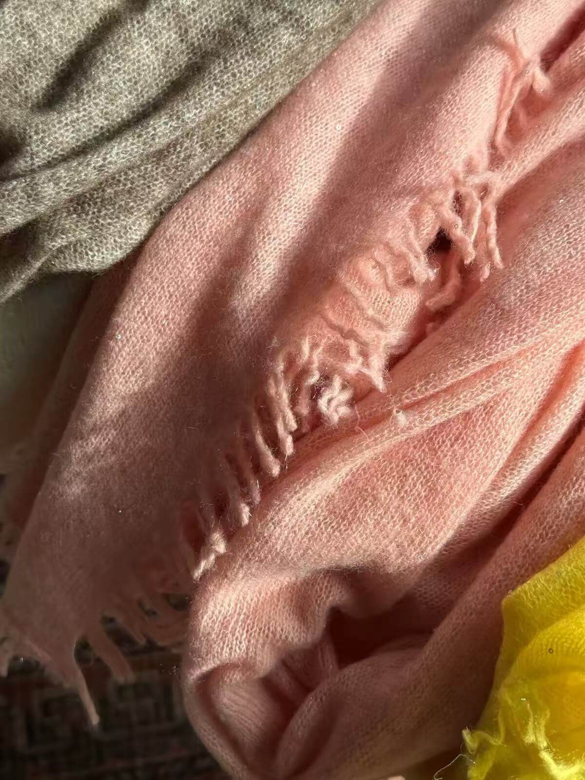 Close-up of pale pink 100% cashmere shawl showing soft knit texture, tiny shimmering sequins and hand-twisted fringe.