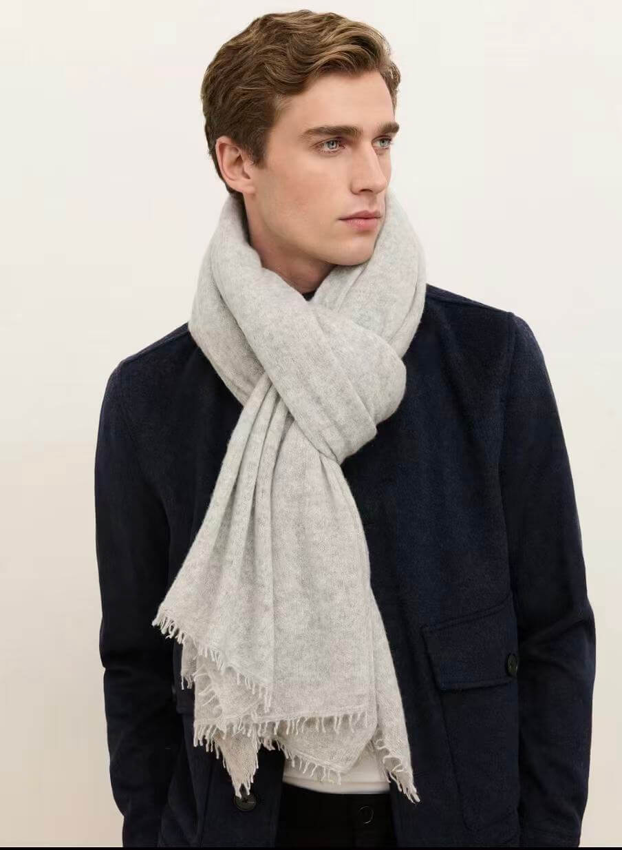 Man styling a light heather gray 100% cashmere scarf with a navy coat, showcasing its oversized drape and fringed edges.