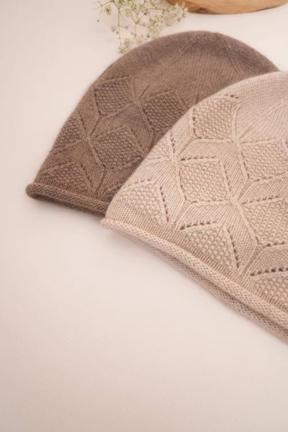 Undyed beige cashmere beanie overlapping a camel hat, showing textured diamond knitting.