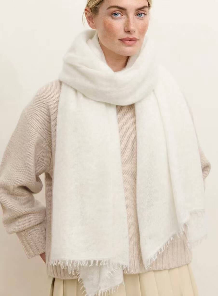 Woman wearing an oversized natural white 100% cashmere scarf with hand-twisted fringe