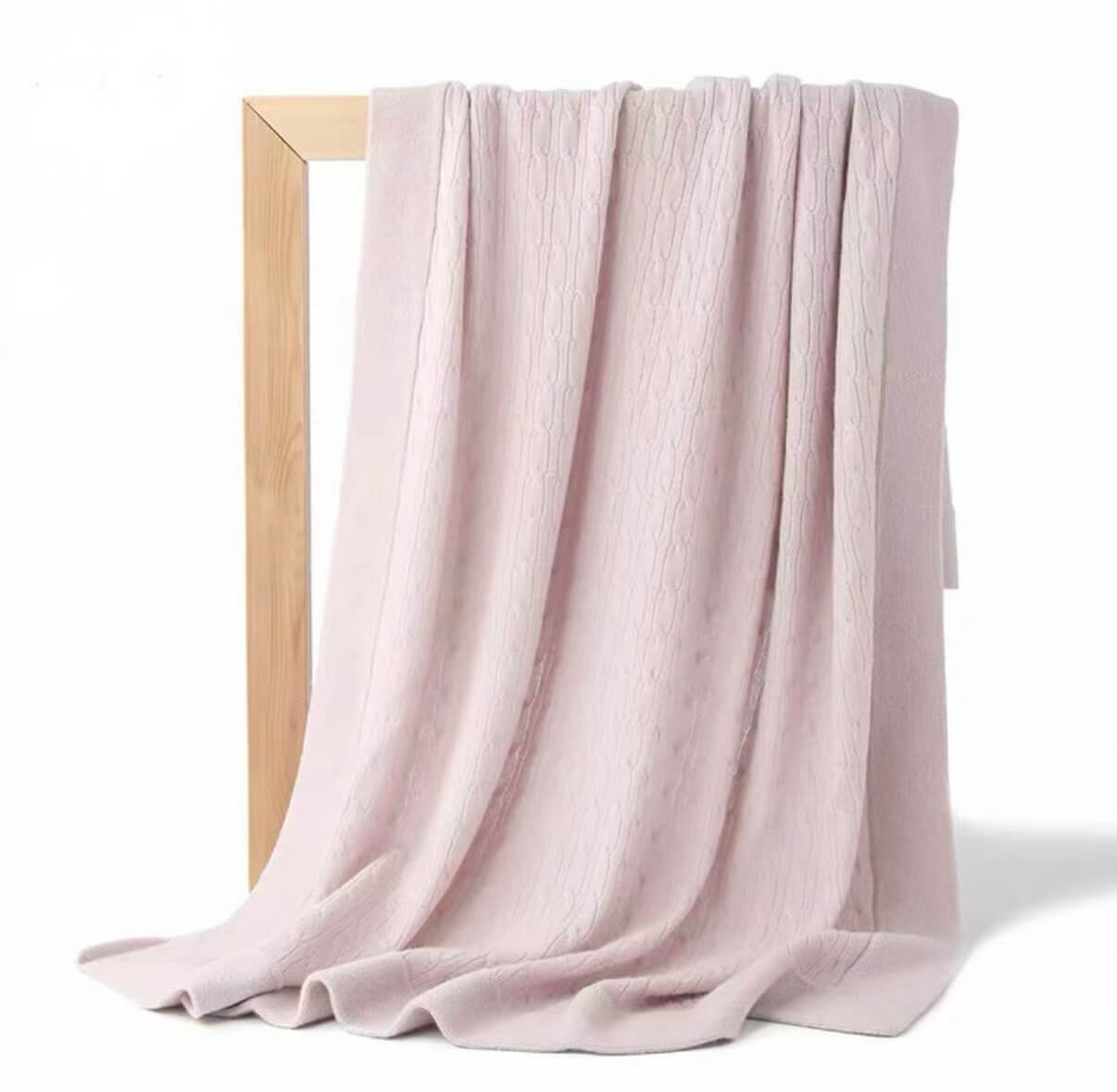 100% cashmere cable knit baby blanket in baby pink, folded neatly on white nursery bed