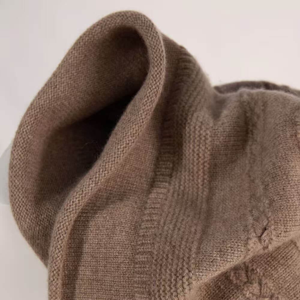 Close-up of a ribbed knit cowl or scarf in a warm taupe-brown color, showing the soft texture and folded edges against a plain light background.