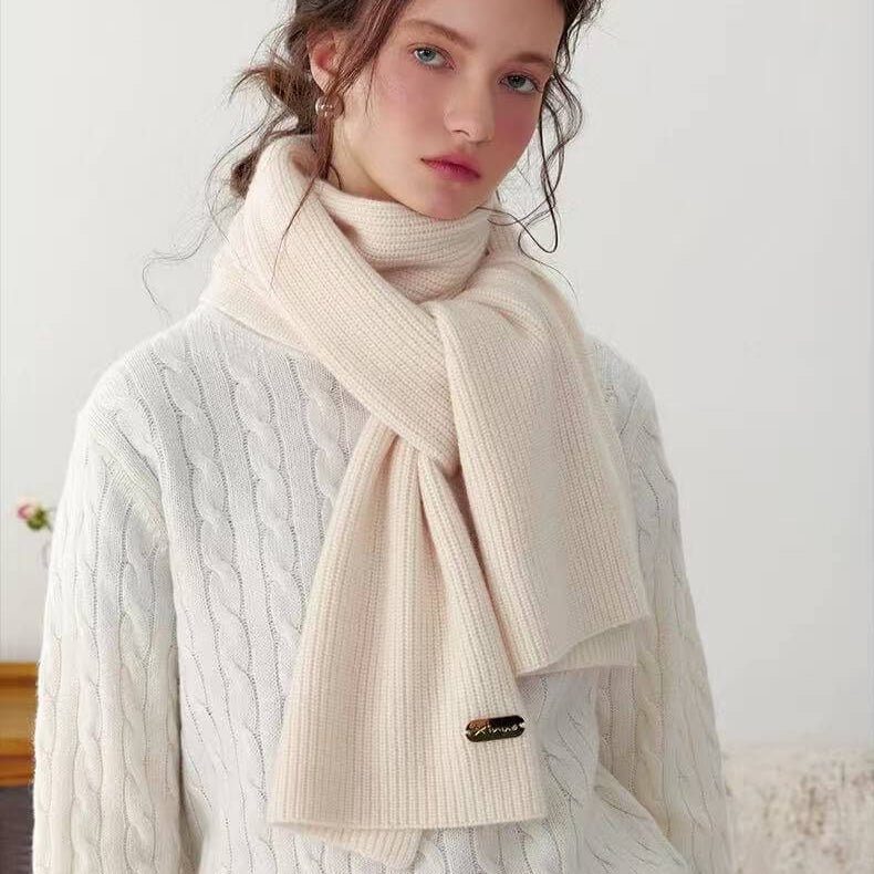 Woman wearing a beige 100% cashmere scarf with a white cable knit sweater against a plain background