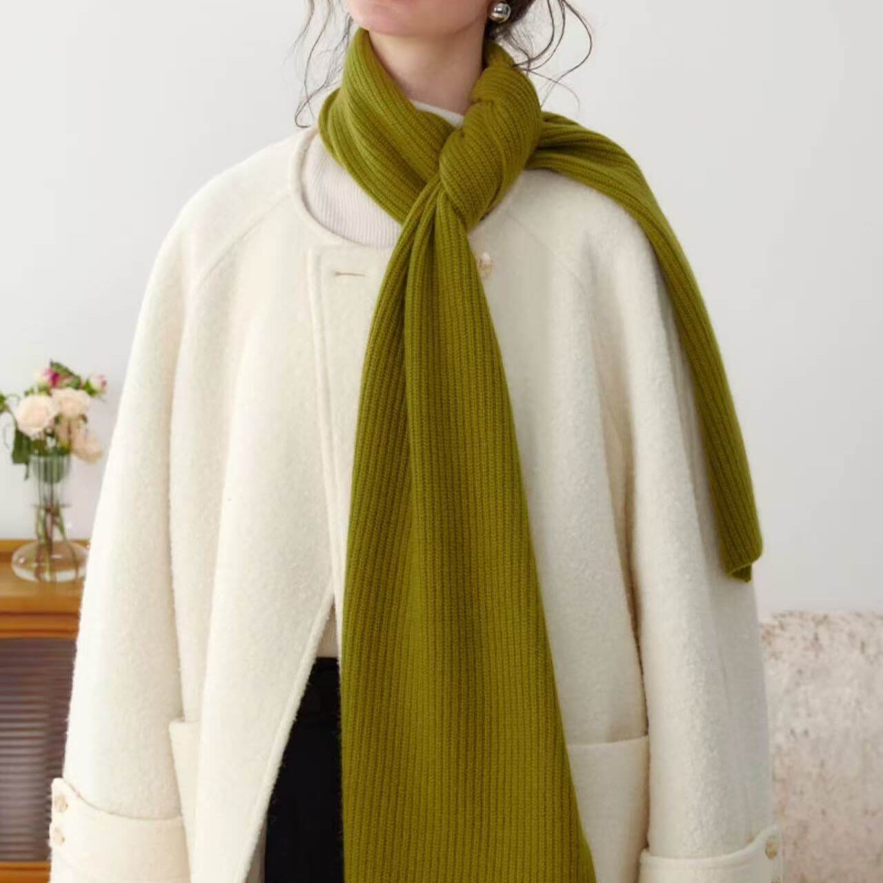 Person wearing a green 100% cashmere ribbed scarf and white coat against a neutral background