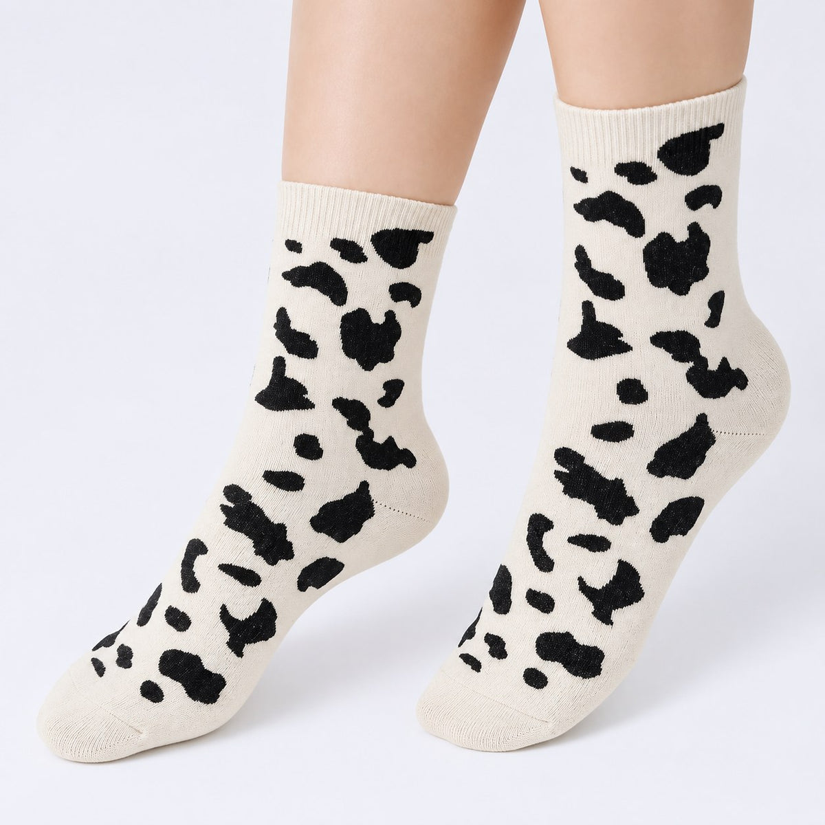 Women's white cashmere-blend crew socks with black cow print, pair worn on feet