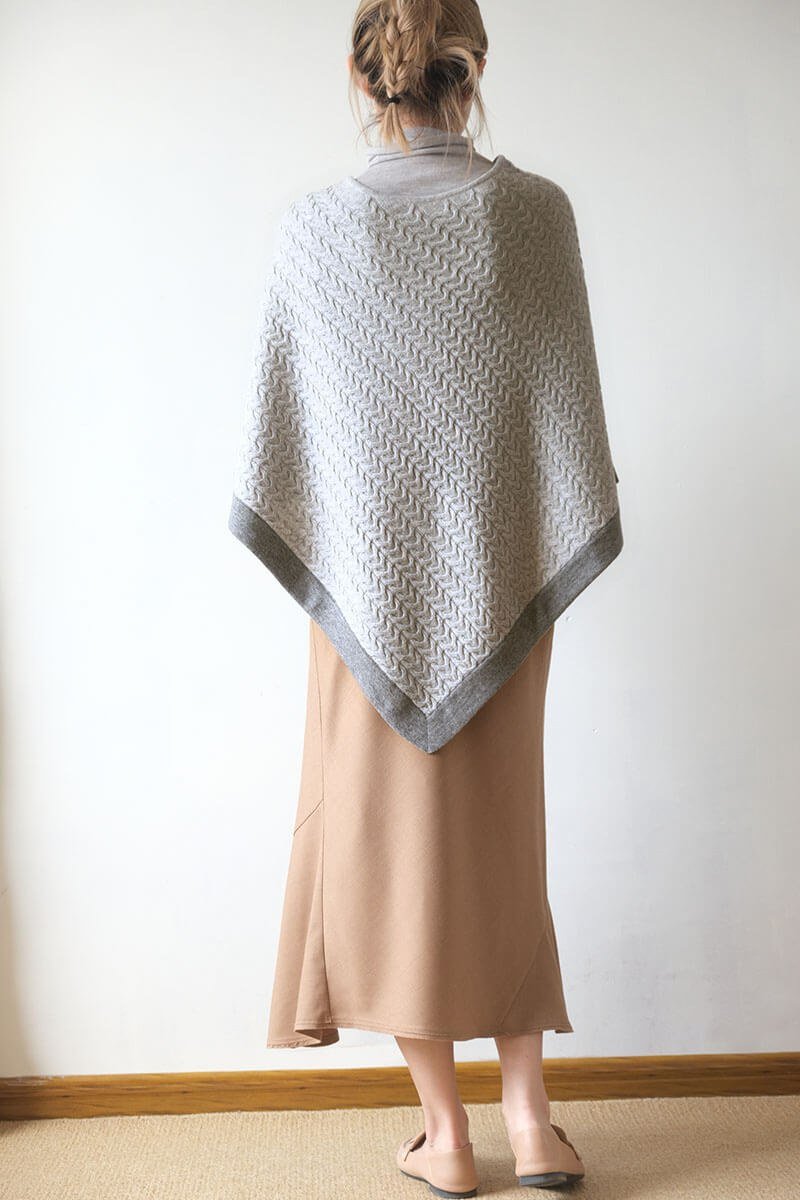 Back view of the two-tone cashmere poncho in light grey with dark grey trim, cable-knit