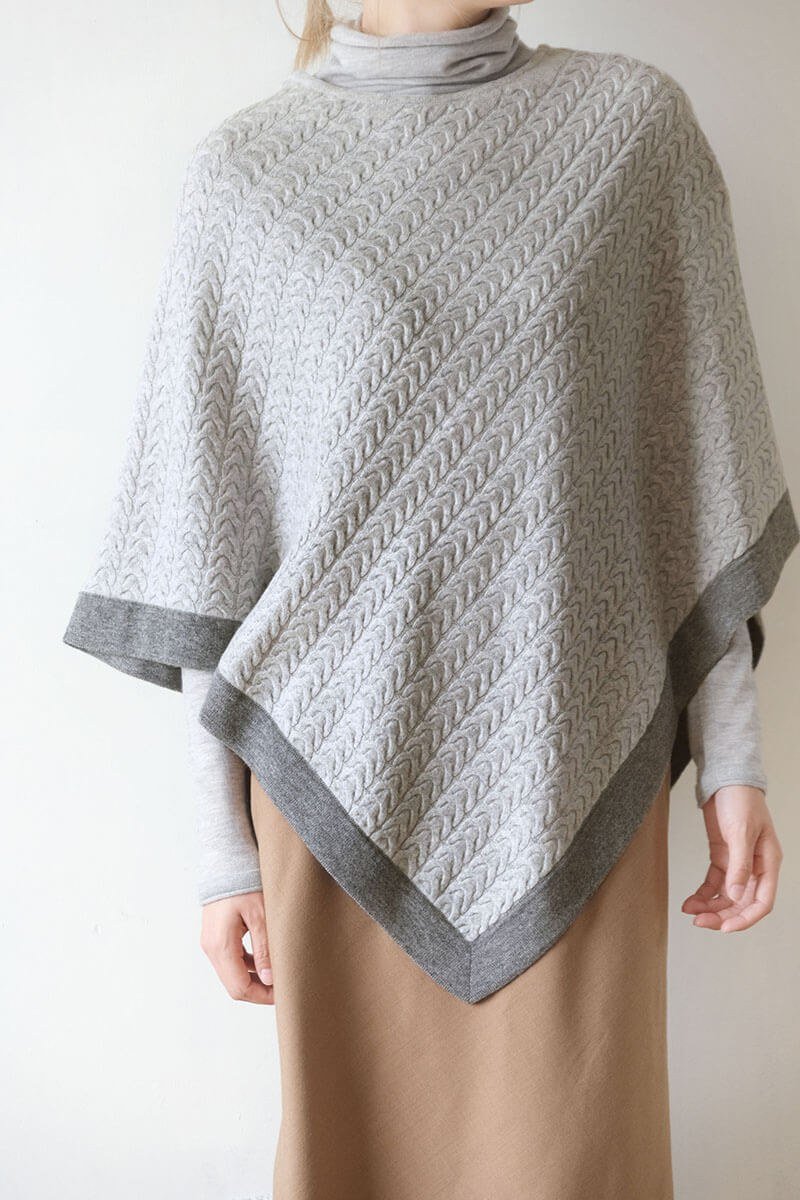 Front view of the two-tone cashmere poncho in light grey with dark grey trim, worn by model