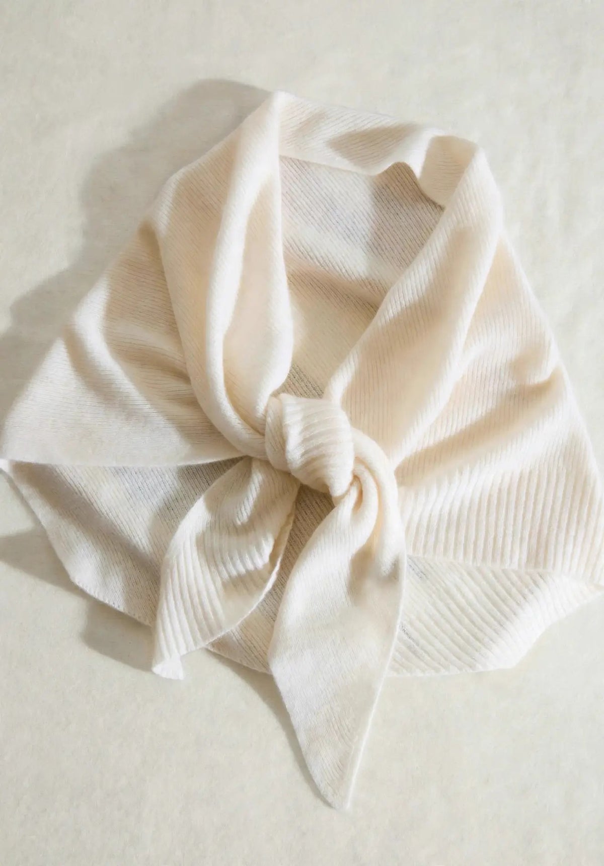 Natural white 100% cashmere triangle scarf styled in an elegant knot, flat lay